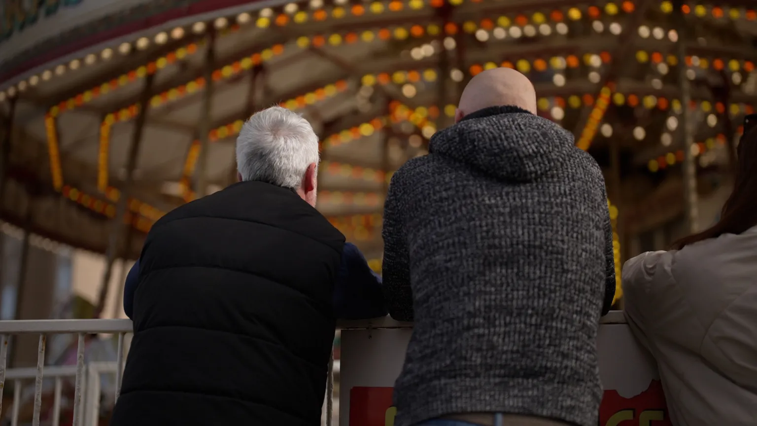 Brijesh Patel/BBC Two men with their backs to the camera look at a funfair carousel
