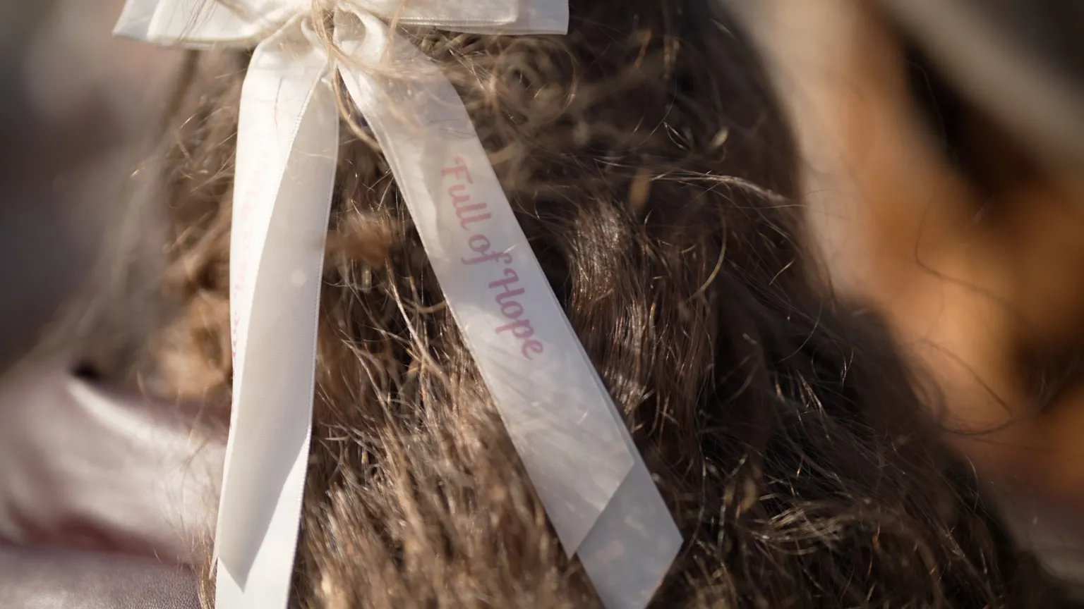 Rob Wood/BBC The back of a girl's head. She has brunette hair with a cream hair bow that has the words 'Full of hope' on it.